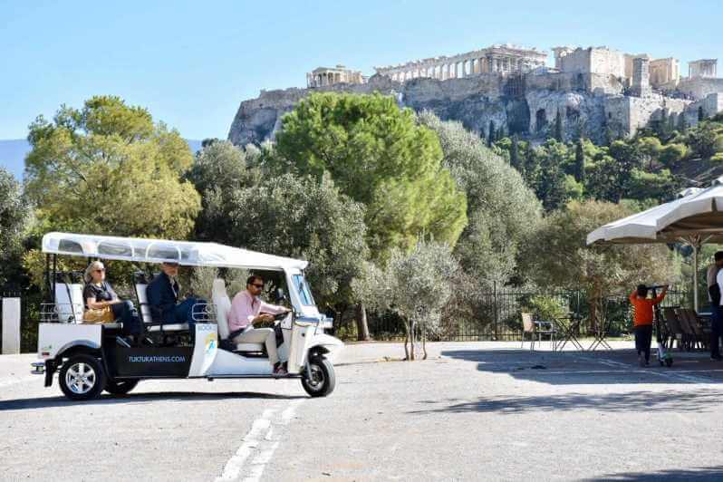 Tourists riding a tuk tuk in athens. Acroplis in the background.